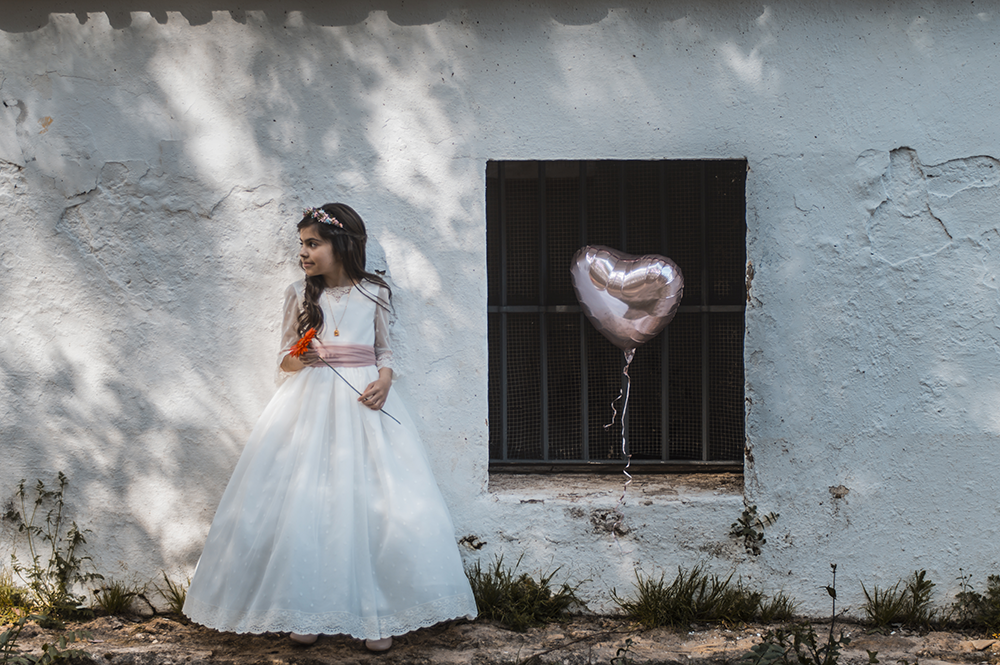 Imagen de Natalia, posando para su reportaje de primera comunión, con globo y flor roja